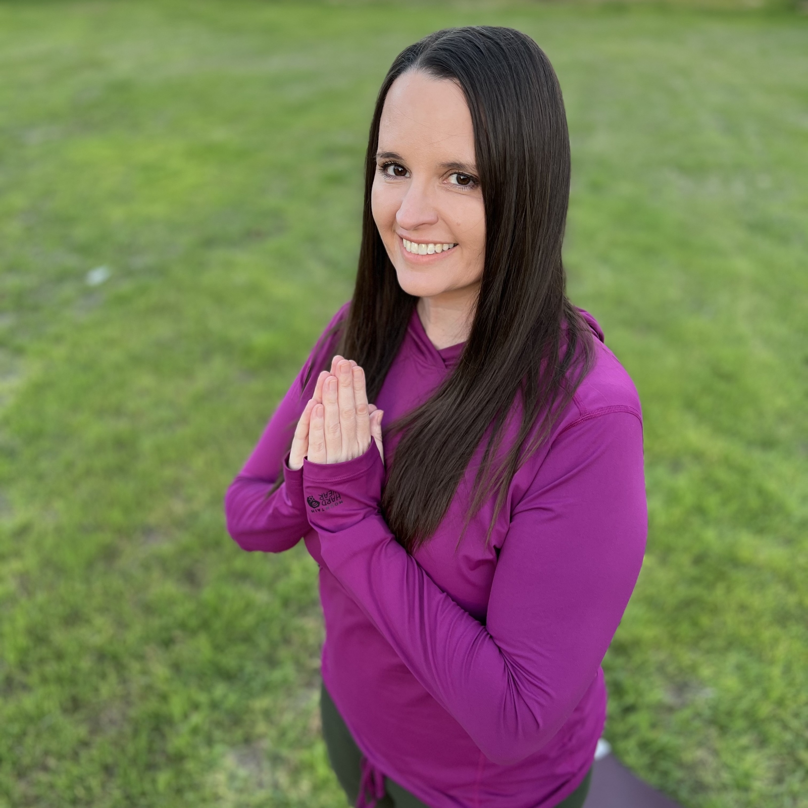 Woman smiling with hands in prayer position outdoors, representing mindfulness, yoga, and positive energy.