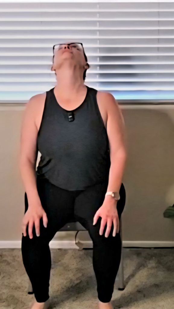 Woman sitting tall in chair cow pose, opening chest and lifting gaze during a desk yoga practice.
