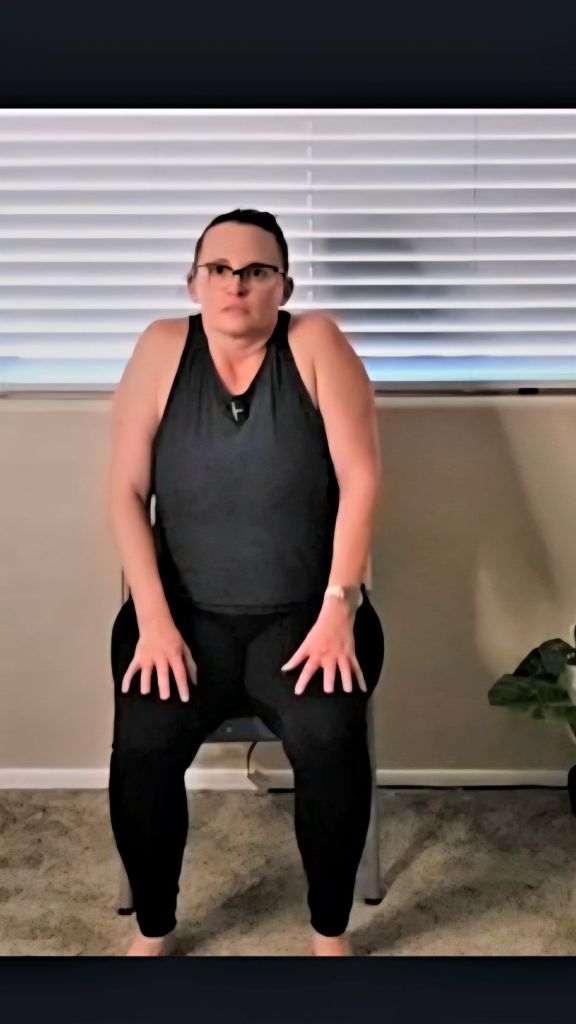 Woman lifting shoulders toward ears in a seated chair yoga pose to release upper body tension at her desk.