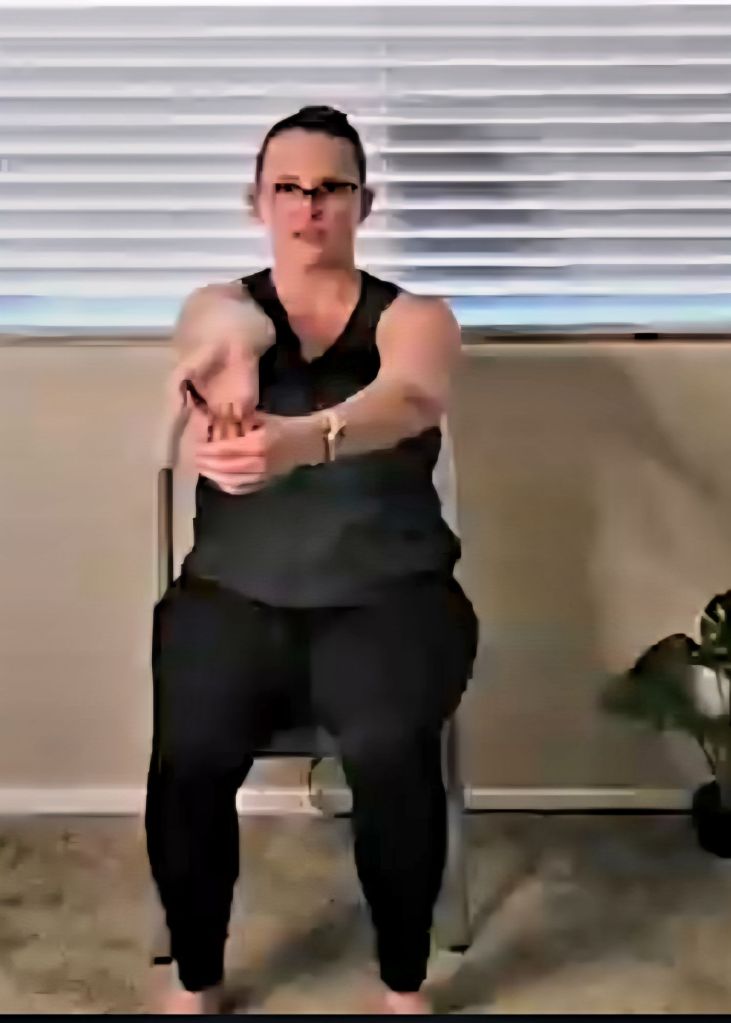 Woman extending arms and stretching wrists while seated to relieve tension from typing and desk work.