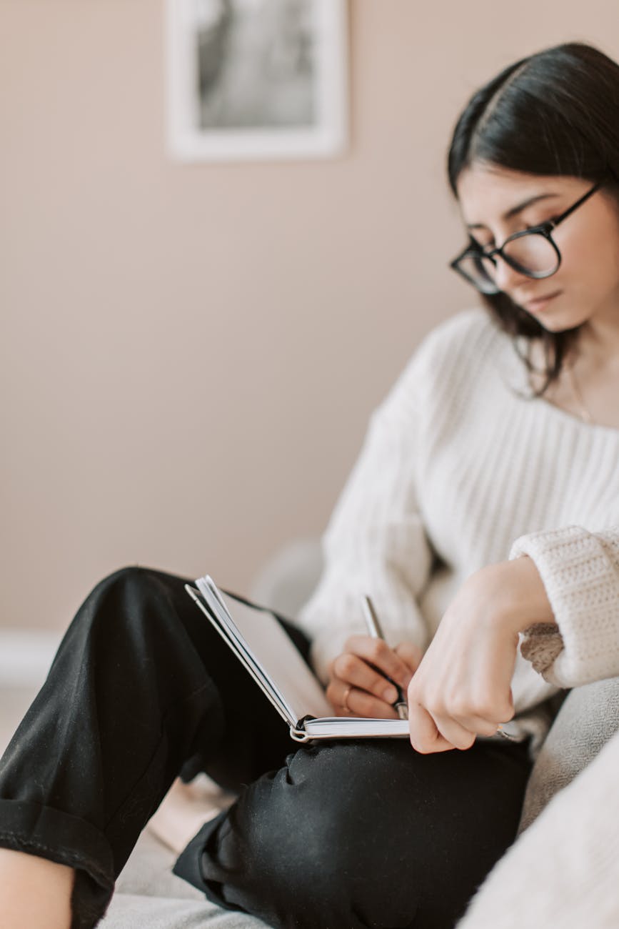 Person sitting indoors writing in a journal, wearing glasses and a cozy sweater, capturing a quiet moment of mindfulness and gratitude during a stressful season.
