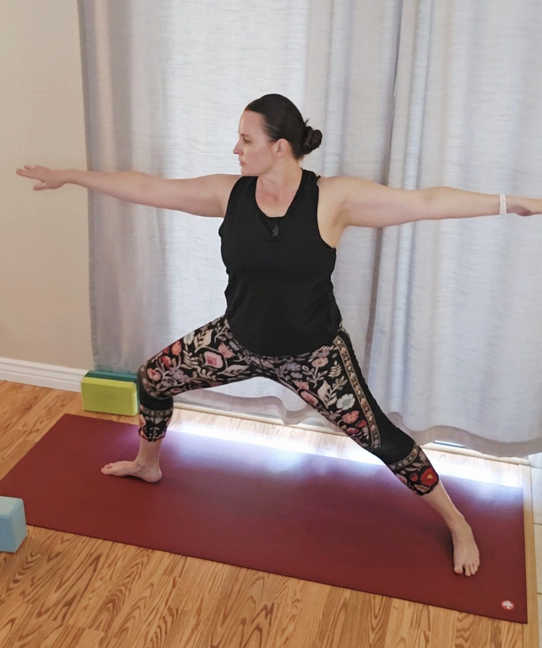 Woman practicing Warrior II yoga pose indoors, demonstrating strength, focus, and balance on a yoga mat.